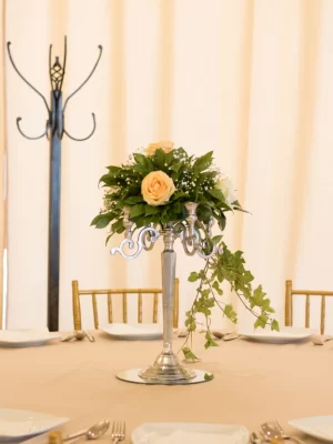 Cvetni aranžman sa krem ružama i zelenilom, postavljen na svećnjaku