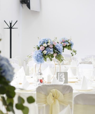 Cvetne ikebane za svadbu sastavljena od plavih hortenzija, roze i belih lizijantusta postavljene na zlatnom prstenu
